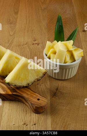 Une tranche d'ananas repose sur une planche à découper en bois. Les tranches d'ananas sont coupées en petits morceaux et disposées dans le bol. Le bol est placé sur un W. Banque D'Images