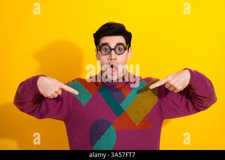 Jeune homme en pull élégant avec expression surprise pointant sur lui-même sur un fond jaune vif Banque D'Images