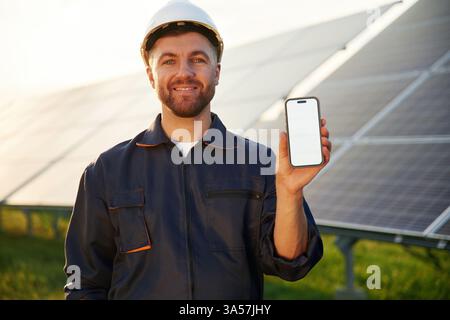Smartphone avec espace de copie. L'homme travaille avec des panneaux solaires à l'extérieur pendant la journée. Banque D'Images