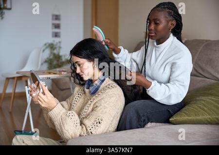 Femme brossant les cheveux d'une amie pendant qu'elle se regarde dans le miroir Banque D'Images