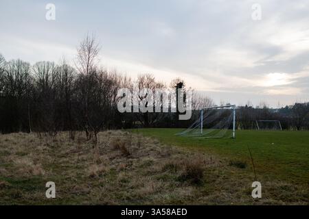 Eham Un terrain de football avec un but et quelques arbres en arrière-plan. Le ciel est nuageux et l'herbe est sèche Banque D'Images