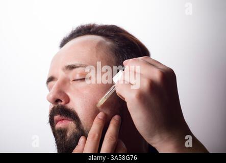 Gros plan du visage masculin et pipette avec une huile pour une croissance de barbe. Banque D'Images
