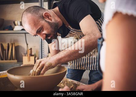Les gens, l'équipe et la poterie dans le studio d'argile, travaillant ensemble et sculptant pour l'artisanat de céramique. Enseignement, équipement et aide à la leçon à l'atelier Banque D'Images