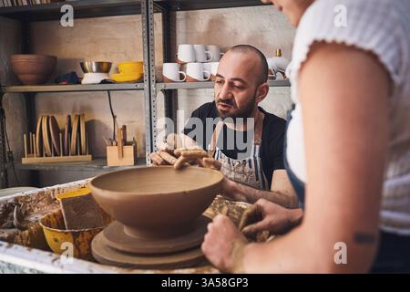 Les gens, l'équipe et la poterie moulent en studio, travaillent ensemble et sculptent de l'argile pour l'artisanat céramique. Enseignement, équipement et aide à la leçon à Banque D'Images