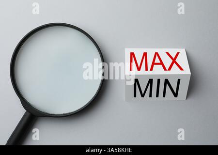 Loupe près de la feuille de papier avec les mots Max et min sur fond gris clair, pose à plat Banque D'Images