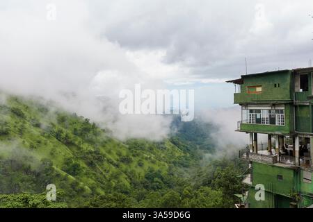 L'image capture les vallées brumeuses d'Ella, au Sri Lanka, avec des montagnes verdoyantes partiellement couvertes de nuages. Un bâtiment à flanc de colline se dresse au bord Banque D'Images