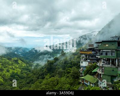 L'image capture les vallées brumeuses d'Ella, au Sri Lanka, avec des montagnes verdoyantes partiellement couvertes de nuages. Un bâtiment à flanc de colline se dresse au bord Banque D'Images