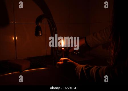 Une fille vérifie l'eau dans un robinet avec une bougie à la main dans un appartement en Ukraine, il n'y a pas de lumière, pas d'eau, les difficultés des gens Banque D'Images