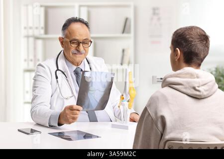 Médecin assis derrière un bureau et vérifiant une radiographie d'un os du genou avec un jeune patient masculin Banque D'Images