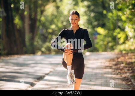 Les jambes s'échauffent. Jeune femme sportive skinny est dans des vêtements de fitness noirs à l'extérieur. Banque D'Images