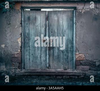 Porte double en bois vieilli dans les tons bleus avec serrure en métal, situé dans un mur de béton délabré dans une ville rurale. Banque D'Images