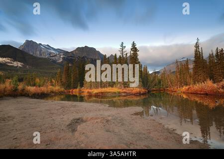 050 lumière de l'aube rougeâtre au-dessus de la rivière Creek-Bow du policier avec les sommets du massif Ehagay Nakoda et de Rundle Range en arrière-plan. Canmore-Alberta-Canada. Banque D'Images