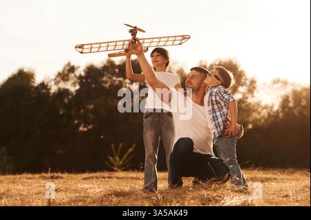 Famille du père, fils et fille jouent avec l'avion jouet en bois sur le terrain. Banque D'Images