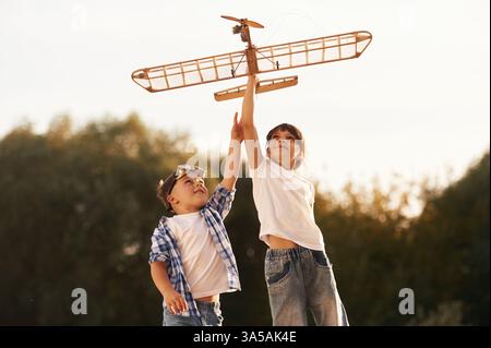 Garçon et fille jouent avec l'avion jouet en bois sur le terrain. Banque D'Images