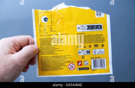 Paris, France - 10 mars 2025 : tient à la main un emballage LEGO en papier déchiré, affiche des informations détaillées sur le produit, des sites de fabrication internationaux, et Banque D'Images