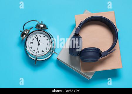 Réveil, livres et écouteurs sur fond bleu clair Banque D'Images