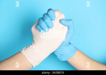 Médecins dans des gants médicaux tenant les mains ensemble sur fond bleu clair, gros plan Banque D'Images