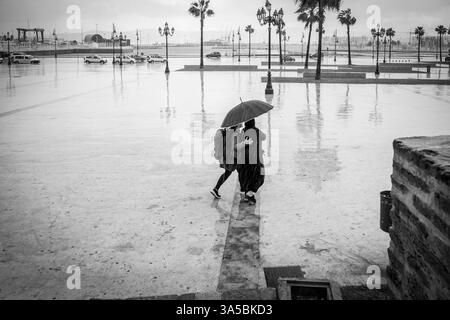 Femmes traversant la place dans les pluies, Tanger, Maroc, Afrique du Nord. Banque D'Images