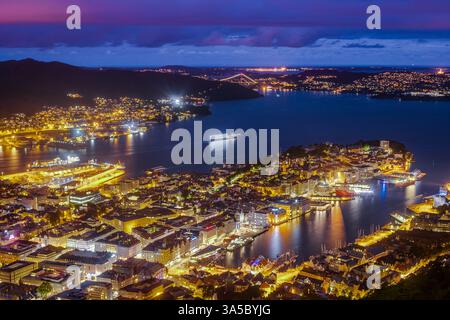 Superbe vue aérienne d'une ville côtière au crépuscule avec des lumières vibrantes reflétant sur les eaux calmes et un paysage urbain illuminé sous un ciel coloré Banque D'Images