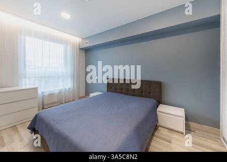 Cette chambre lumineuse et contemporaine présente des murs bleus, un mobilier élégant et une ambiance calme. L'espace est bien éclairé par la lumière naturelle et expose Mo Banque D'Images