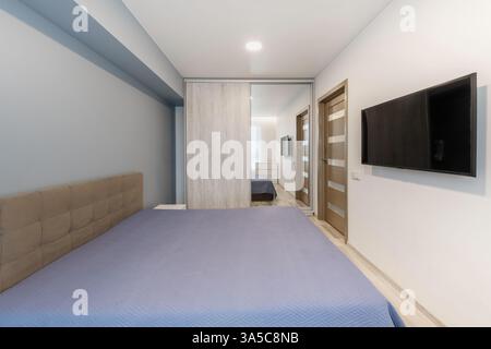 Intérieur lumineux de la chambre au design moderne, avec lit confortable, télévision et lumière naturelle à travers des rideaux translucides. Un calme et minimal Banque D'Images