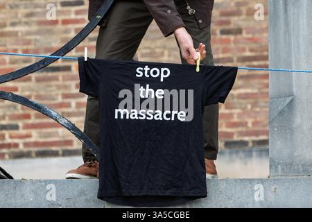 Bristol, Royaume-Uni. 22 mars 2025. Un partisan pro-palestinien est photographié accrochant des T-shirts « arrêtez le massacre » sur les rampes devant l'hôtel de ville de Bristol avant une marche de protestation pro-palestinienne dans le centre-ville de Bristol. La marche de protestation et le rassemblement d'urgence 'End the Genocide, Ceasefire Now !' ont été organisés par divers groupes de soutien palestiniens de Bristol, la coalition Bristol STOP the War et le Bristol Trades union council. Crédit : Lynchpics/Alamy Live News Banque D'Images