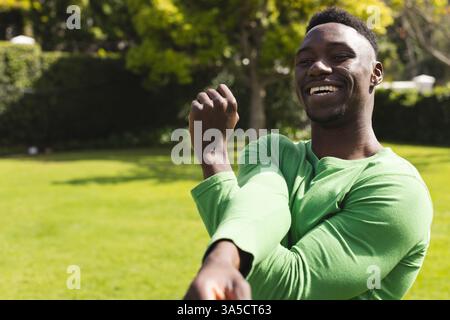 Homme afro-américain étirant les bras dans le parc, souriant et profitant de la journée ensoleillée, copiez l'espace Banque D'Images