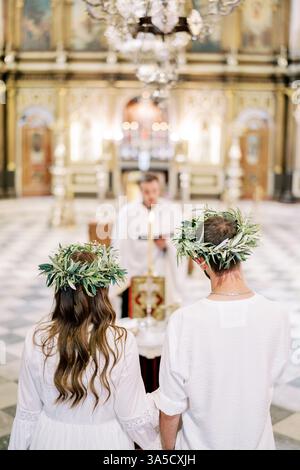 Monténégro, Kotor - 07 juillet 2024 : mariés et mariés en couronnes se tiennent devant le prêtre menant la cérémonie de mariage. Vue arrière Banque D'Images