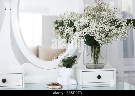 Bouquet de belles fleurs de gypsophila et branches d'eucalyptus dans un vase sur une coiffeuse près du miroir à l'intérieur Banque D'Images