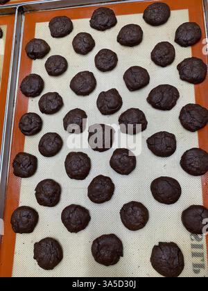 Des dizaines de boules de pâte à biscuits au chocolat sont disposées soigneusement sur un tapis de cuisson, en attendant leur tour dans le four pour une friandise sucrée. Banque D'Images