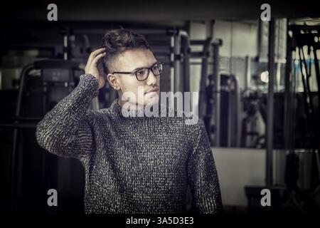 Beau jeune homme asiatique blanche portant chandail gris, debout dans l'obscurité Banque D'Images