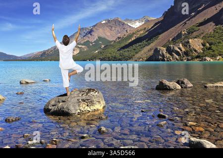 Yoga sur le lac. La femme mature en blanc exécute l'arbre d'asana, debout sur un rocher Banque D'Images