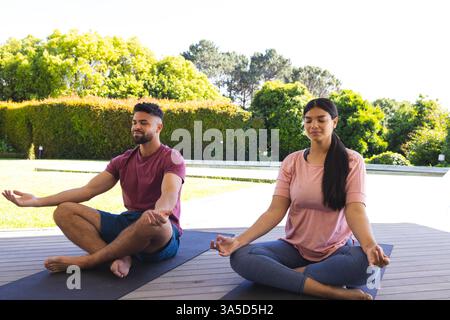 Couple méditant à l'extérieur sur des tapis de yoga, profitant d'un cadre paisible de jardin Banque D'Images