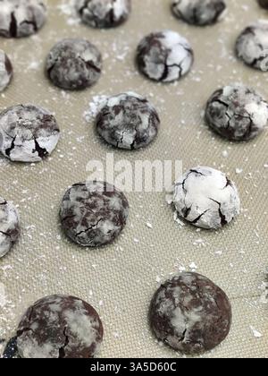 Biscuits froissés au chocolat avec du sucre en poudre refroidissant sur un plateau, mettant en valeur leur surface craquelée et texturée dans une cuisine chaude. Banque D'Images