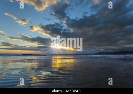 Lever du soleil sur l'océan. Les couleurs douces des nuages se reflètent dans l'eau de l'océan. Un vent léger provoque de petites ondulations dans l'eau. Les rayons du soleil font leurs Banque D'Images