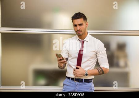 Beau jeune homme à son bureau tapant et using cell phone, de graves Banque D'Images