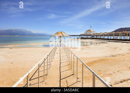 Les garde-corps enferment le chemin vers l'eau. Beau parapluie rond protège du soleil. Le lac salé sans drainage au moyen-Orient. Mer morte. Côte de l'est Banque D'Images