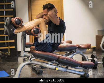 Beau jeune homme musclé travaillant, exerçant les jambes sur l'équipement de gymnastique Banque D'Images