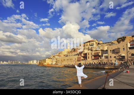 Coucher de soleil sur le Vieux Jaffa à tel Aviv. Port de jetée de pêche, la femme en blanc effectue Asana Tree sur une jambe Banque D'Images