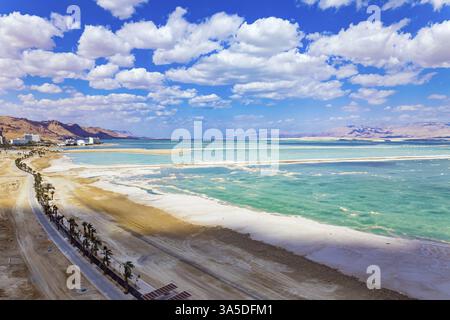Mer morte. L'eau reflète le bleu vif du ciel. Les nuages de cumulus luxuriants se reflètent dans l'eau. Images de drone. Autoroute bordée de palmiers Banque D'Images