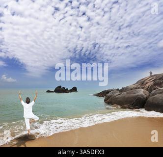 Thaïlande. Magnifique plage sur la mer d'Andaman. Femme d'âge moyen habillée en blanc faisant du yoga Banque D'Images