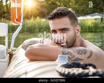 Portrait d'un jeune homme beau barbu avec un corps tatoué regardant sexuellement la caméra naviguant en bateau Banque D'Images