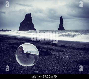 L'eau de mer froide roulant sur le sable humide près de falaises de pierre rugueuse sur jour de tempête sur la plage noire Reynisfjara qui jouit en Islande Banque D'Images