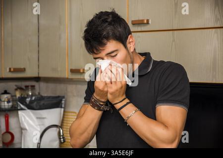 Jusqu'à la taille d'un jeune homme avec des allergies ou froid soufflé dans les tissus du nez En Étant Debout dans la cuisine Banque D'Images