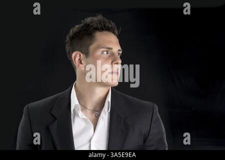 Portrait de la tête et des épaules d'un jeune homme séduisant sérieux en chemise blanche et veste regardant sur le côté, isolé sur fond noir Banque D'Images