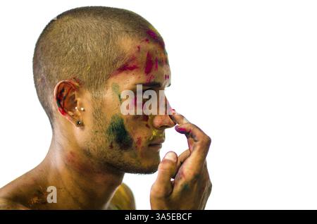 Vue latérale de l'homme avec le visage peint appliquant des poudres de couleur holi. Isolé sur fond blanc. Gros plan Banque D'Images