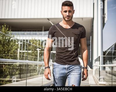 Un beau jeune homme décontracté dans un cadre urbain moderne dans la ville européenne, marchant et regardant la caméra Banque D'Images