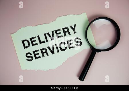Livraison services texte écrit sur papier avec loupe plate sur fond rose Banque D'Images