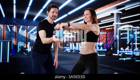 Entraîneur de fitness aidant la femme dans l'entraînement kettlebell à la salle de gym. Banque D'Images
