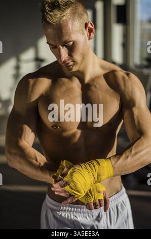 Muscular young man wrapping bandage autour de ses mains pour l'entraînement de boxe Banque D'Images